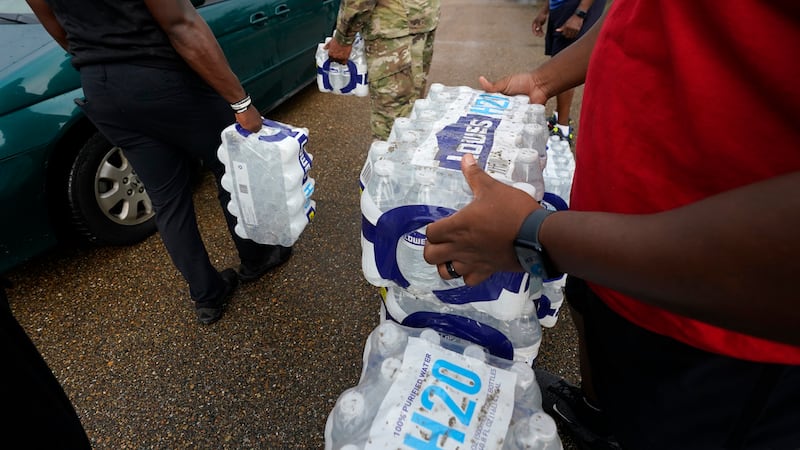 FILE - Volunteers distribute cases of water at a community/fraternal drive-thru water...